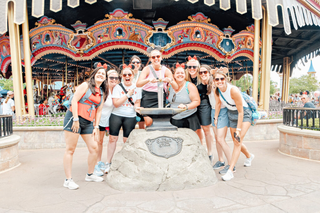 group of women at sword and stone in front of magic kingdom's Prince Charming carousel 